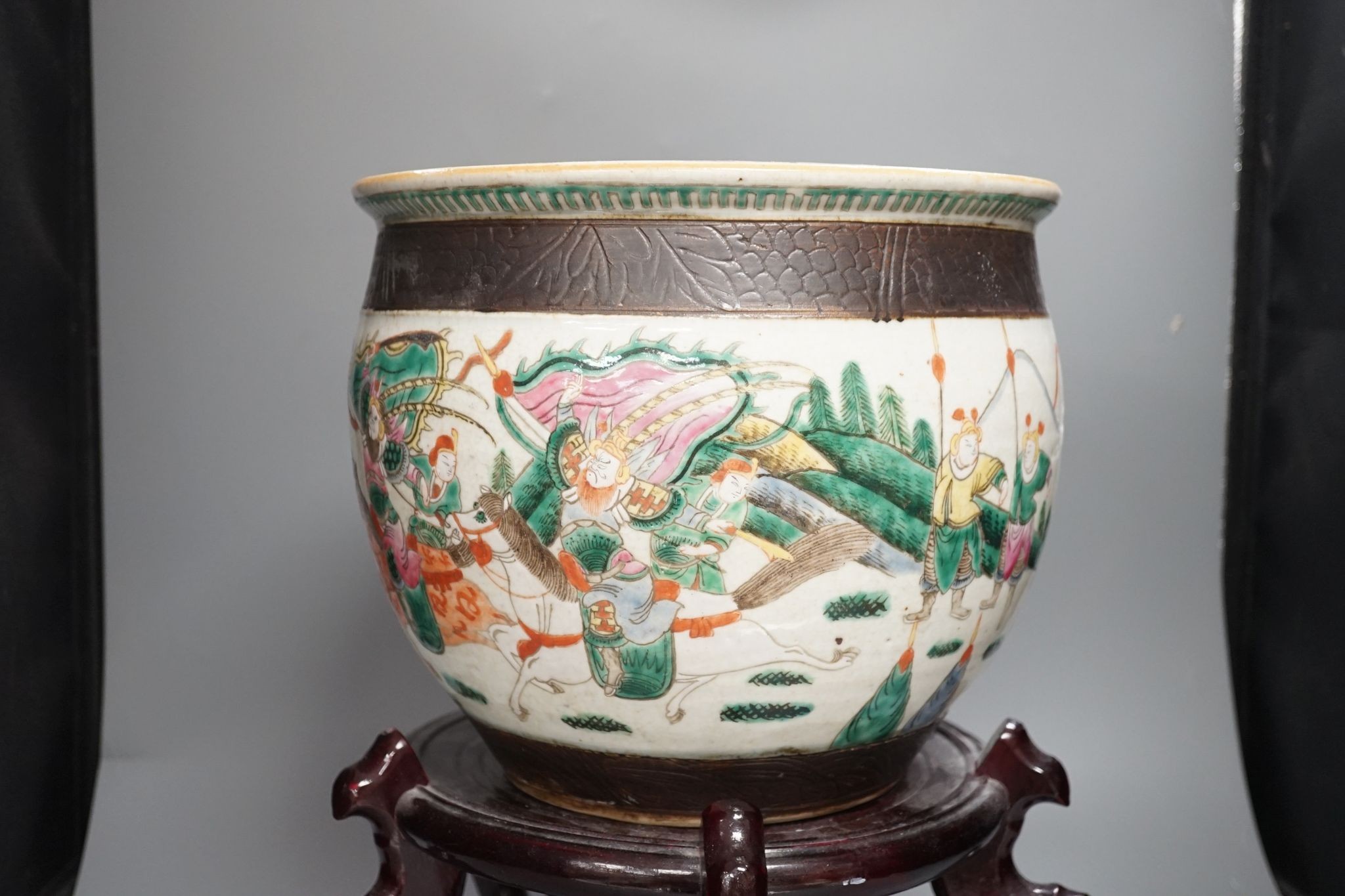A Chinese famille rose ‘warriors’ jardiniere, late 19th century, wooden stand, 42 cms high including stand.